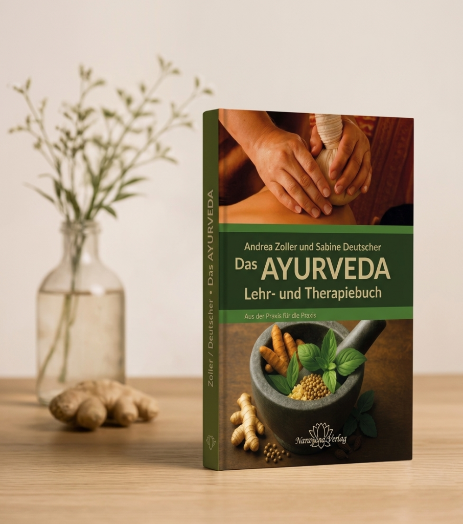 Das Buch „Das AYURVEDA Lehr- und Therapiebuch“ steht auf einem Holztisch neben einer Ingwerwurzel und einer kleinen Vase vor einem hellen Hintergrund.
